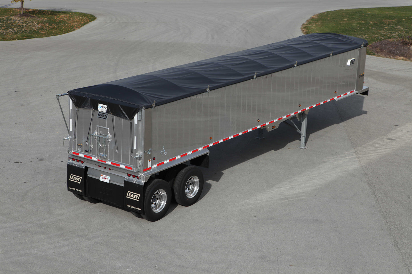 End dump trailer equipped with a Kwik‑Lock roll tarp system, showing a black tarp covering the load on an aluminum trailer parked on a paved lot, viewed from an elevated rear‑side angle.