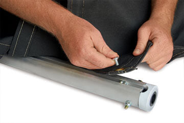 Hands fastening a tarp to an aluminum winder bar, demonstrating installation of a truck tarp roll system on a white background.